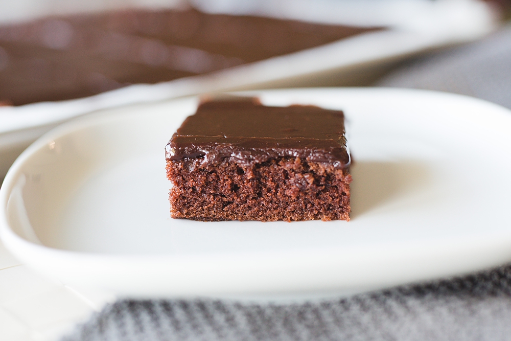 Slice of chocolate sheet cake with thick layer of shiny old fashioned fudge icing, dairy-free and rich in cocoa flavor.
