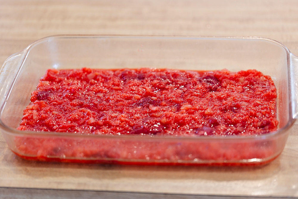 Red strawberry jello mixture with fruit being poured into a greased 9x13 pan.