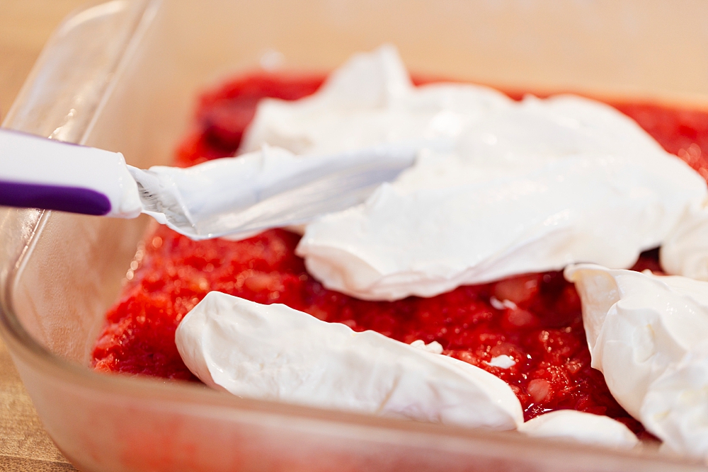Spreading sour cream evenly over firm jello layer in a glass baking dish